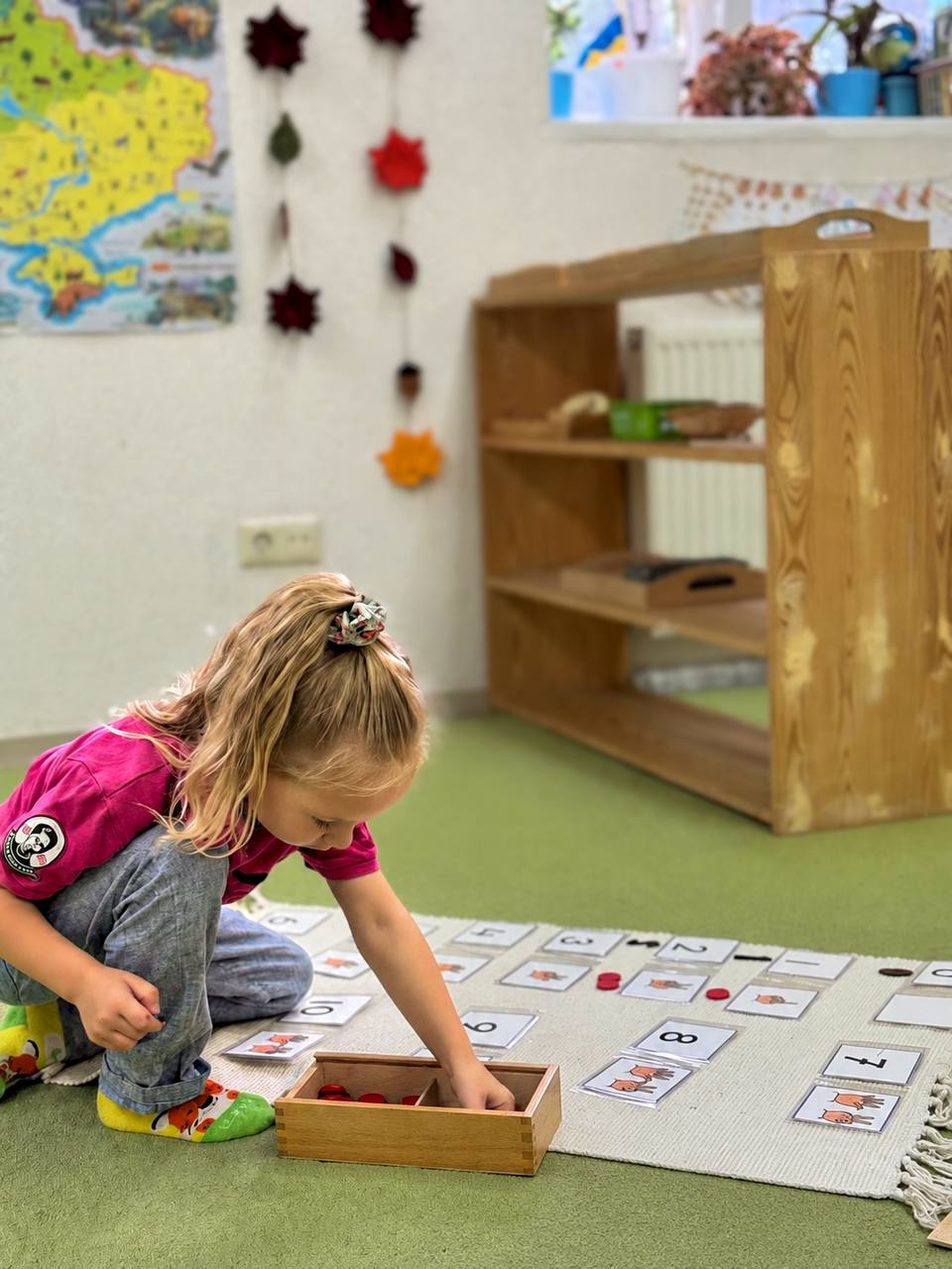 Дівчинка розкладає числа й фішки на килимку в старшій групі