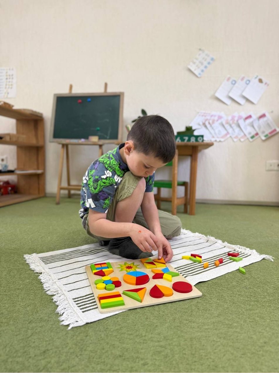 Хлопчик складає пазл на зеленому килимі в групі KidsCan