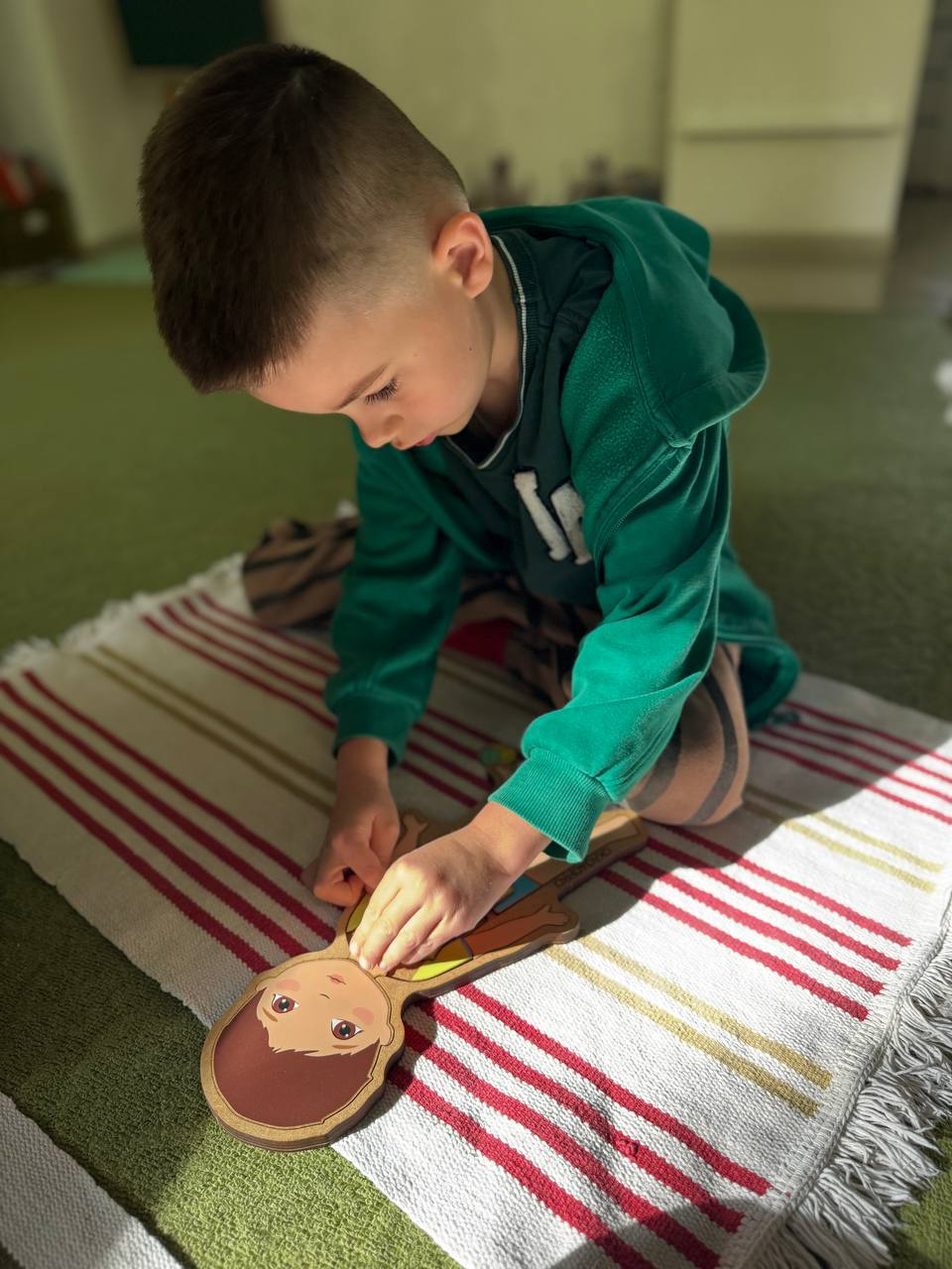 Хлопчик складає дерев’яний пазл на килимку в групі KidsCan